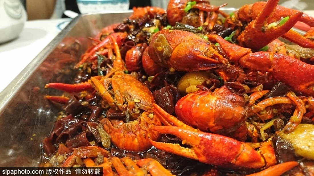 Spicy crayfish gives Guijie its visual punch: red shells, chile oil, gloves, beer, and a table that refuses to stay tidy.