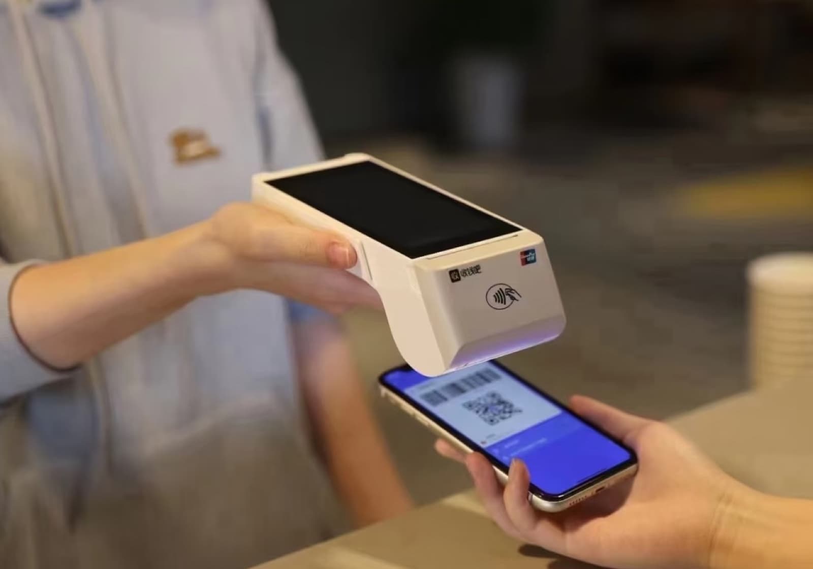 A cashier scanning a customer's phone payment code with a handheld POS terminal