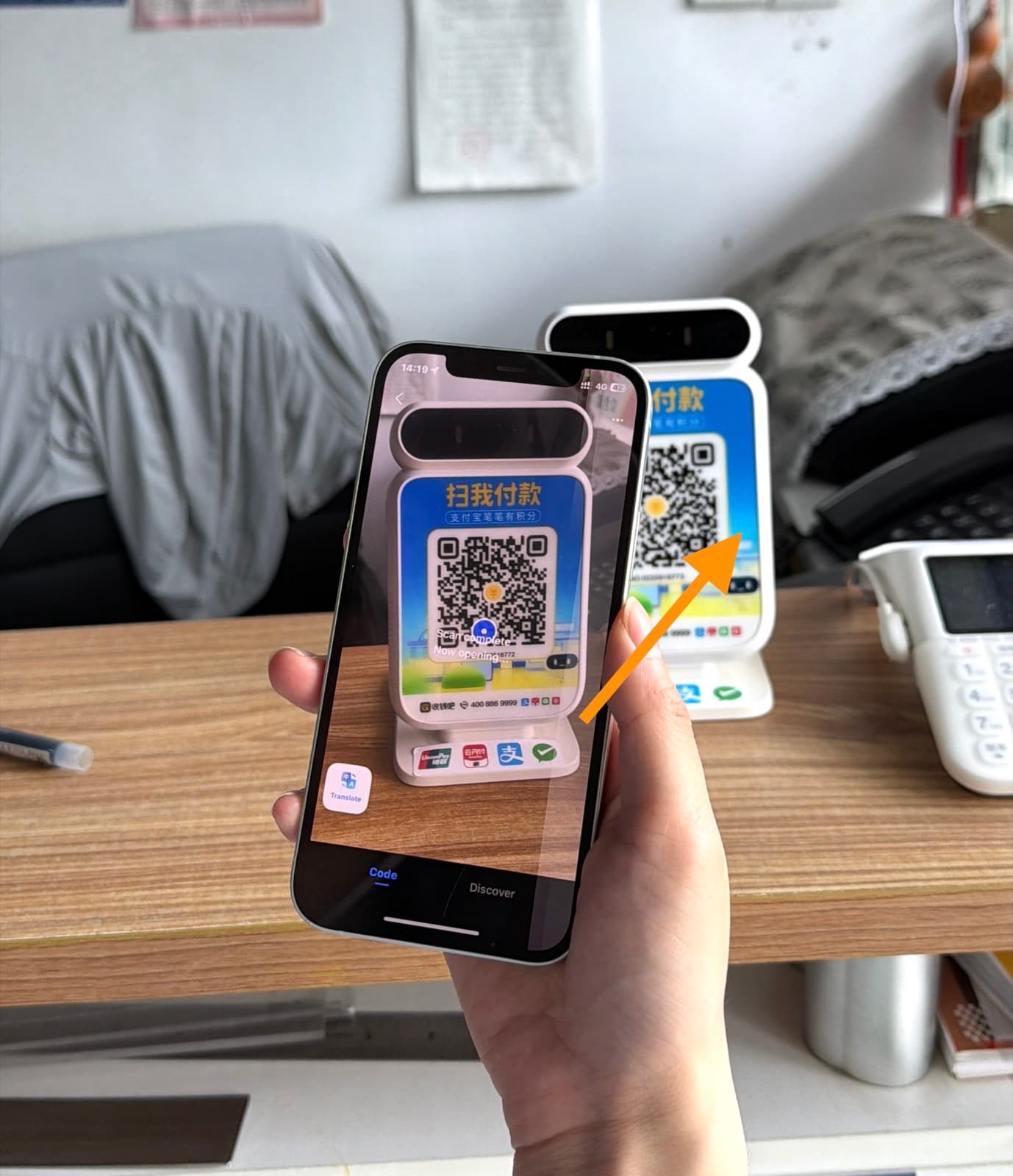 Phone camera scanning a merchant's blue QR code standee on a shop counter
