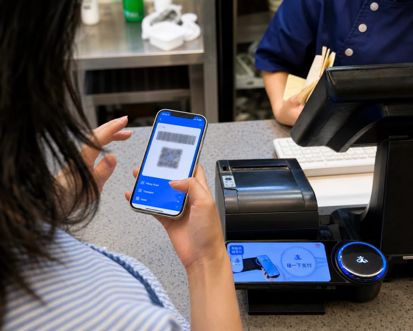 A phone displaying an Alipay payment code at a counter