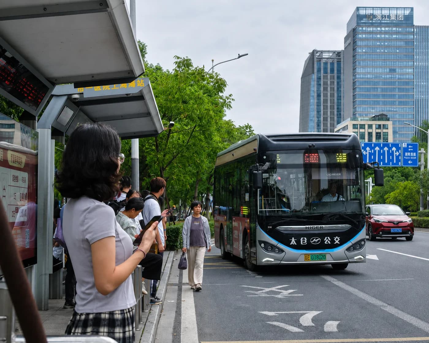 Yadi checking her phone at a bus stop as a bus approaches