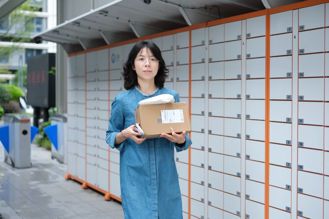 Yadi holding a parcel beside delivery lockers