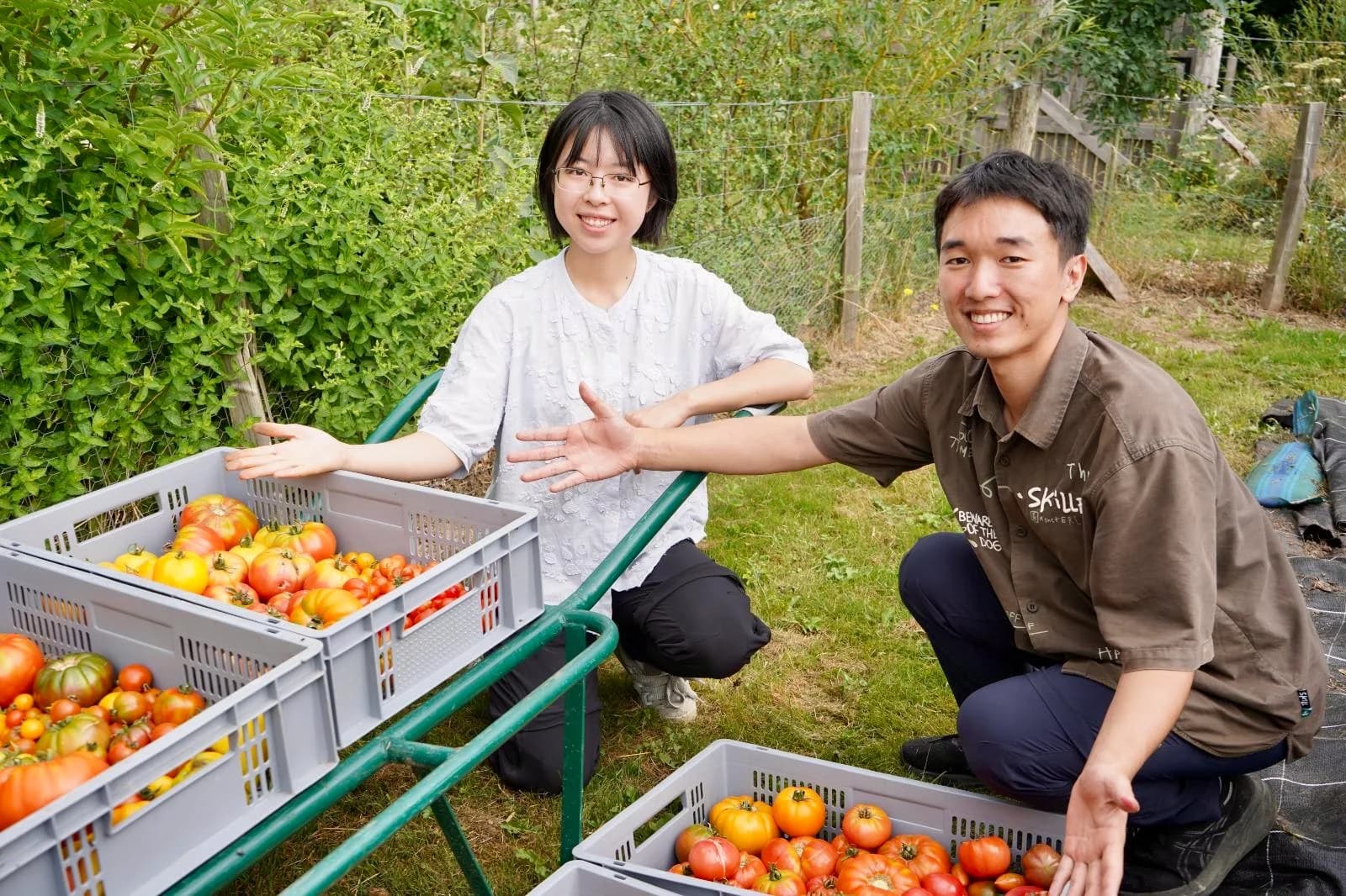 Will and Yadi smiling beside crates of tomatoes in a garden